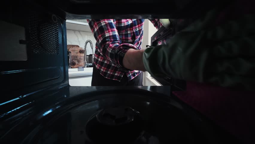 Man In Rubber Protective Gloves Cleaning The Inside Walls Of A Microwave Oven In The Kitchen