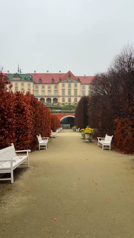 A stroll on a cloudy day through the manicured garden path lined with benches leading to Royal Castle in Warsaw, Poland. Ogrody Zamkowe