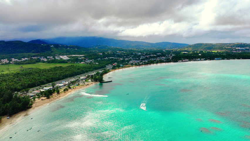 Picturesque landscape of the Atlantic coast on the island of Puerto Rico. Recreational boats on turquoise water. Panorama of a sandy beach and mountains covered with forests.