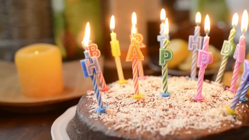 Close-up of a birthday cake with lighted candles and “Happy Birthday” inscription, capturing a warm celebratory mood with soft lighting and festive party atmosphere.