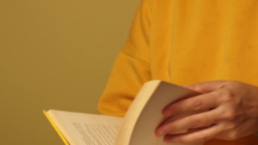 Woman in yellow clothes turning yellowed pages of old book. Concept of learning, knowledge, education and studying.