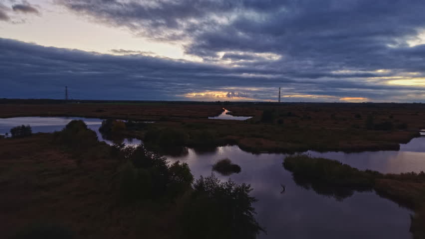 As the sun sets, dark clouds gather over tranquil wetlands, reflecting in the winding rivers below. A peaceful scene captures the beauty of twilight, inviting calm.