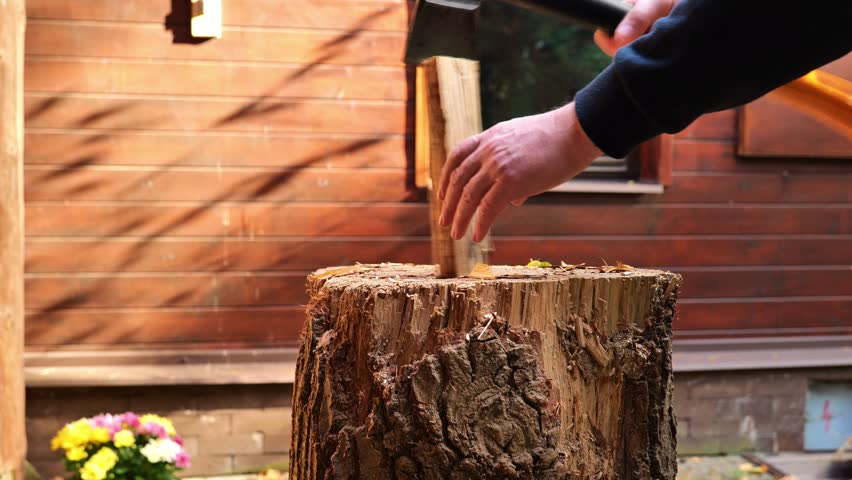 The process of chopping firewood.splitting wood with an axe against a wooden house background. Heating season. 4k footage