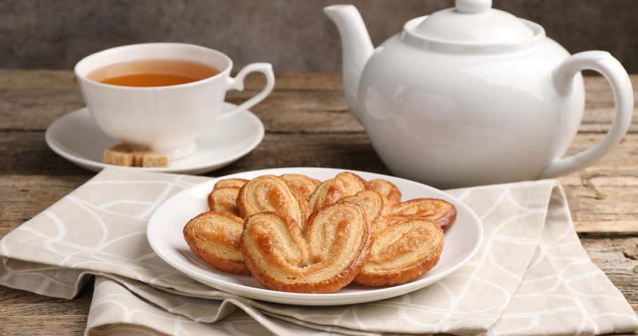 Woman taking palmier cookie at wooden table, closeup