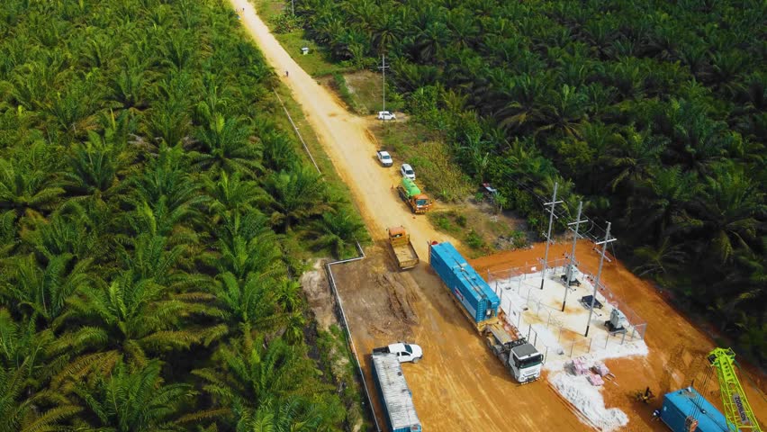 Cinematic Drone Footage of Onshore Drilling Rig equipment structure for oil exploration and exploitation in the middle of jungle surrounded by palm oil trees during sunset and high oil price 4k