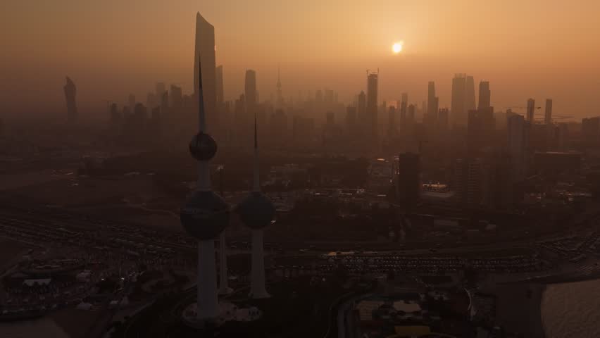 Cinematic drone view of Kuwait City at sunset: Kuwait Towers in silhouette, sun over hazy skyline, warm golden light, no people—perfect for travel, tourism, city timelapse intros, and skyline B-roll.