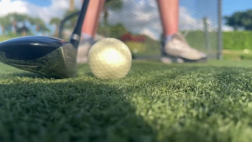 A Slow motion close up of a Golf ball being hit by a Driver on a Driving range in a sunny and green location