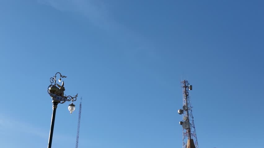 Communication towers and vintage lamp post under blue sky