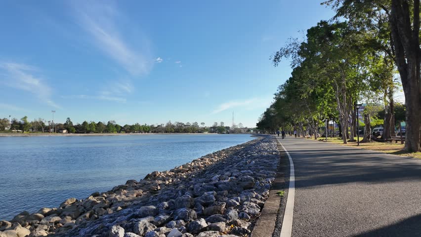 Stone covered lake shore path with trees and blue sky