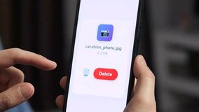 A closeup shot of a mans hands holding a smartphone, with a prompt on the screen to delete a photo file. He presses the delete button, and a notification confirms that the files have been successfully - Powered by Shutterstock - Get 15% off with code: PIKWIZARD15