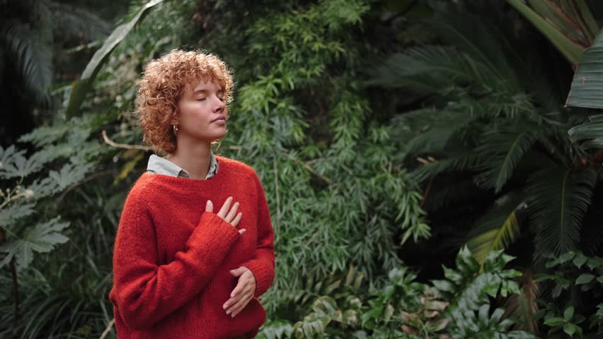 Relaxed young redhead woman with eyes closed breathing outside in nature in meditation. Tranquility and relaxation concept. Person in peace and harmony 