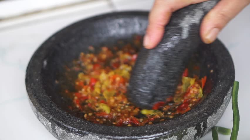 Close-up of red chili being crushed in a stone mortar, showcasing authentic Asian cooking and traditional food preparation