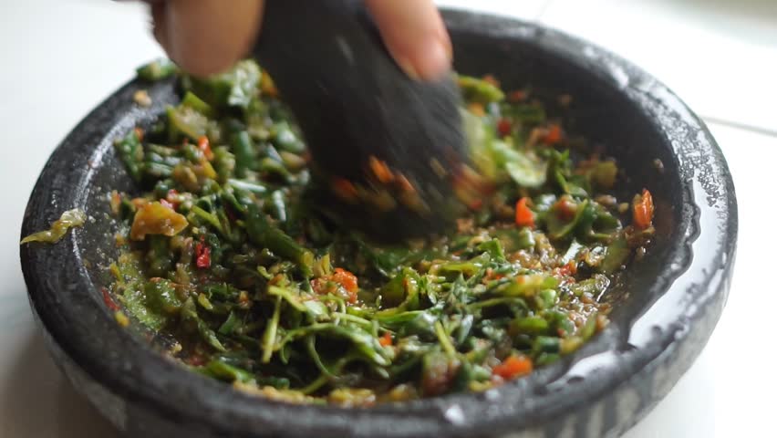 Close-up of long bean salad with red chilies crushed in a stone mortar, showcasing authentic Asian cuisine and traditional food preparation.