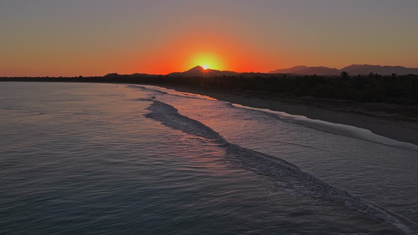 Sunrise over a tropical beach in Miches. The orange sun rises behind a mountain, reflecting on the ocean waves. Ideal for travel and nature concepts