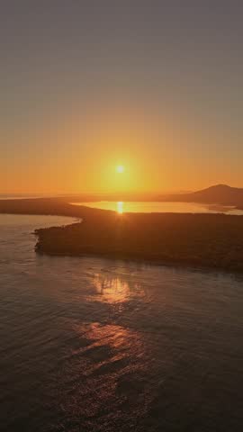 Vertical shot of a golden sunrise over Miches Bay. The sun's reflection shimmers on the water, silhouetting the tropical coastline. Ideal for social media travel reels and inspirational content