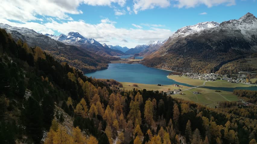 breathtaking aerial dolly in of vivid alpine landscape in Engadin Valley, Switzerland in fall featuring forests, snow capped mountain peaks, green meanows and lakes