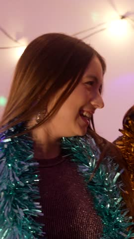 Two cheerful female friends in festive costumes laughing and toasting with colorful cocktails, enjoying a vibrant house party atmosphere during a new year