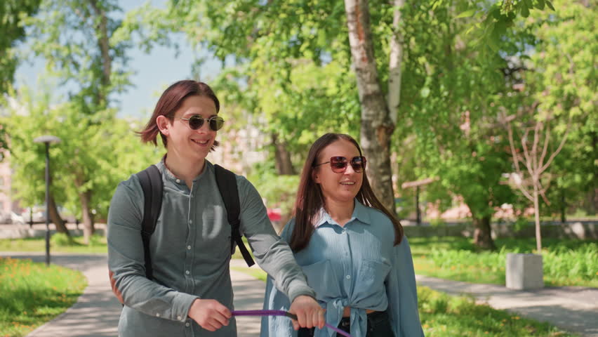 fashionable pair with canine outdoors, stylish couple casually strolling with their dog beneath leafy trees, fashionable pair savoring relaxed walk with their pet under shade of tall trees