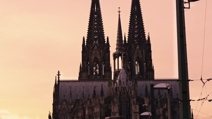 A classic architectural view of the world-famous Cologne Cathedral seen through the heavy-duty steel structure of the Hohenzollern Bridge.