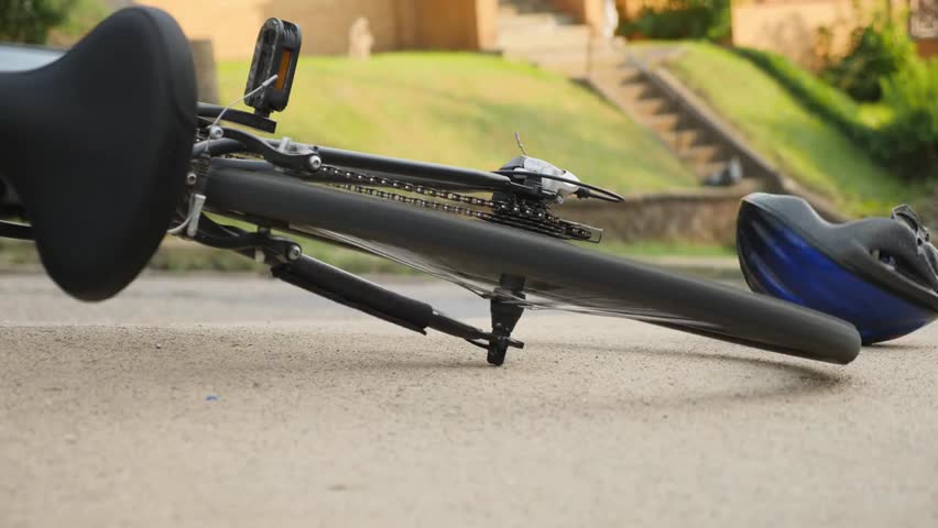 A bicycle lies on the sidewalk with spinning wheels after an accident, as traffic passes by, illustrating urban hazards, street safety, and unexpected incidents.