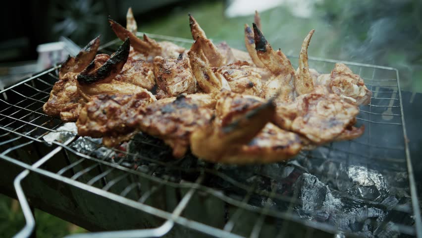 Crispy Chicken Wings Grilling On Barbecue Wire Rack Over Hot Charcoal. Marinated Meat Poultry Roasting On BBQ Grate With Smoke, Summer Picnic Food. Savory Grilled Chicken Parts For Outdoor Dinner BBQ