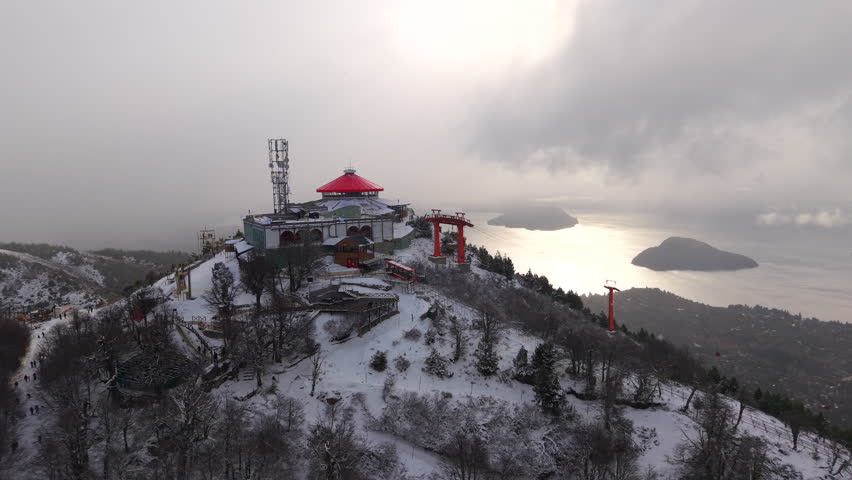 Amazing drone orbit around Cerro Otto snowy mountain peak with cable car station overlooking winter landscape, San Carlos de Bariloche, Río Negro, Argentina