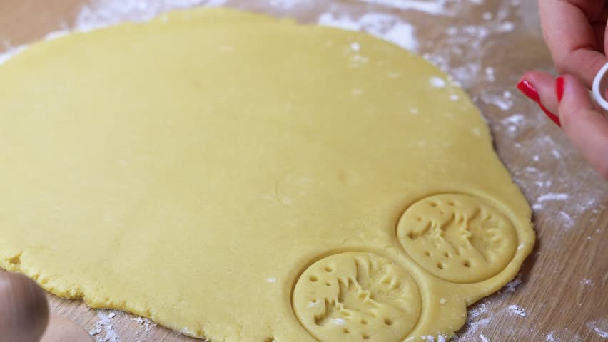 Detailed view of hands using a cookie cutter on rolled dough. The scene captures the precision and artistry of biscuit making, set in a cozy kitchen environment.