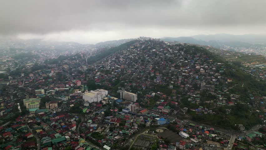Panoramic aerial orbit of densely populated hillside community Quirino Hill overlooking Baguio City, Philippines during overcast day