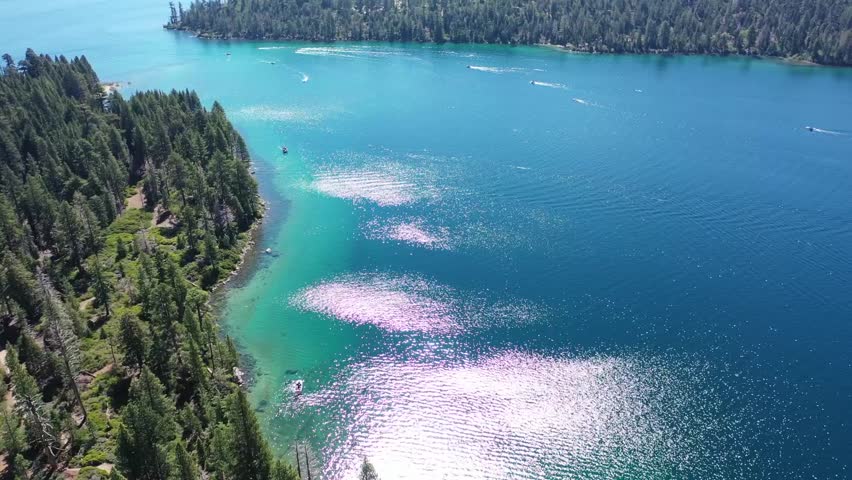 Drone flyover of Emerald Bay shoreline off of lake Tahoe California. Green waters of the shoreline with boats in the distance.