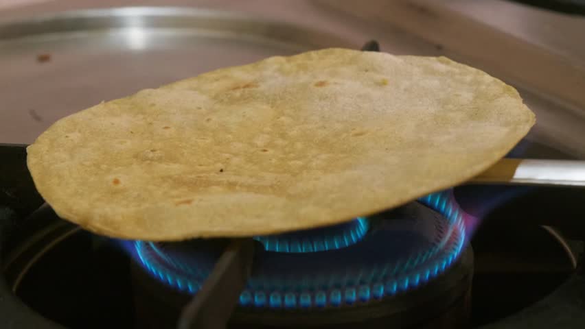 Close-up shot of a pulka (phulka) puffing up directly over a gas stove flame at home. internal shot, stable shot, 4k.
