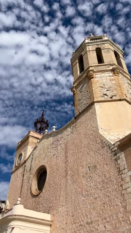 Église de Sant Bartomeu i Santa Tecla. A historic Catholic church. Dominating the Passeig de la Ribera skyline in Sitges. Catalonia. Spain. Under a striking blue sky filled with white cumulus clouds.