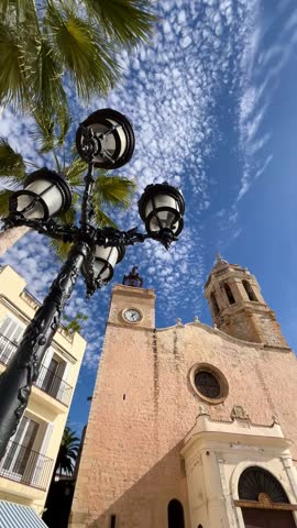 Église de Sant Bartomeu i Santa Tecla. A historic Catholic church. Dominating the Passeig de la Ribera skyline in Sitges. Catalonia. Spain. Under a striking blue sky filled with white cumulus clouds.