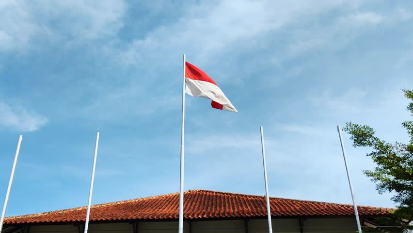 Indonesian flag flying in front of building under blue sky