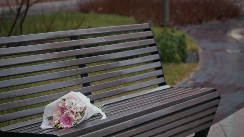 Late young woman taking bouquet from wooden bench and starting texting her boyfriend