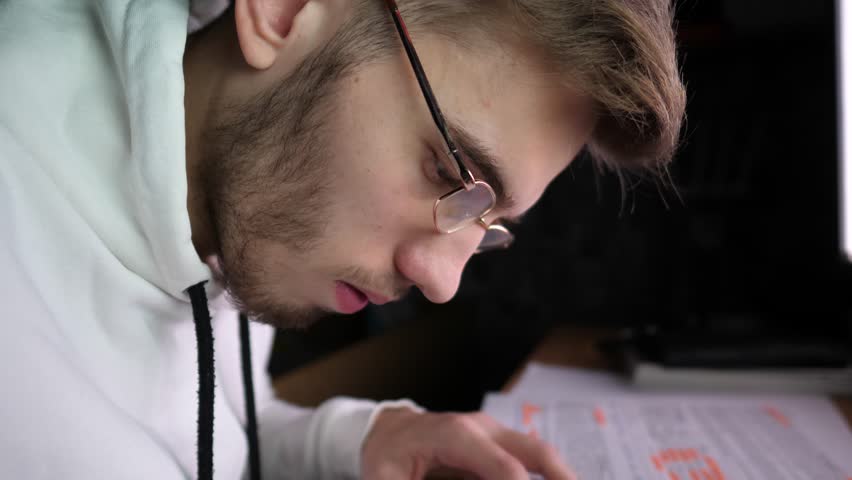 Male broker writes data on paper after analyzing foreign exchange graphs at computer. Young financial analyst making notes in notepad at evening time. Concept of bitcoin BTC and stock market. Slow mo