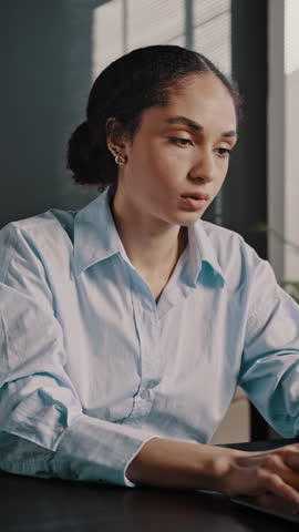 Stressed African American woman holding head in hands, feeling demotivated while sitting at office desk and online working on laptop. Portrait of exhausted multitasking executive director at workplace