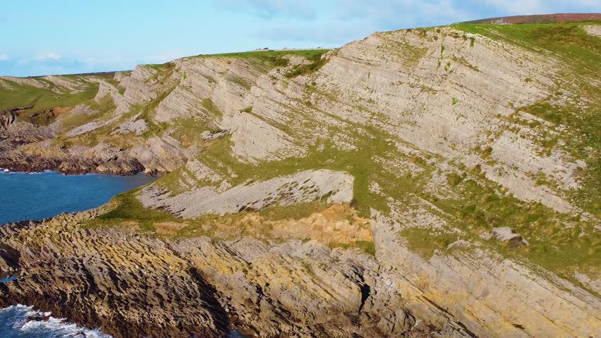 Orbiting Aerial View of Scenic Welsh Coastline with Hilltop House in Background with Stone Wall Lining Coast Path. Travel Nature Drone Clip. Beautiful Welsh Gower Peninsula.