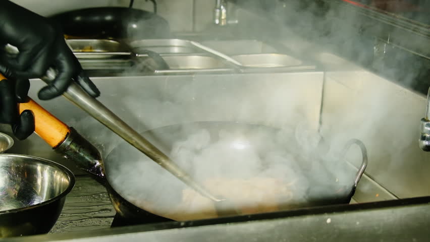Cook stirs noodles while tiny flames lick the curved wok. Station handles rush orders for travelers and late night delivery in busy Vietnam city
