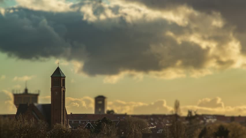 Miniature style timelapse of a european city district at golden hour featuring a church steeple and water tower under fast moving clouds.