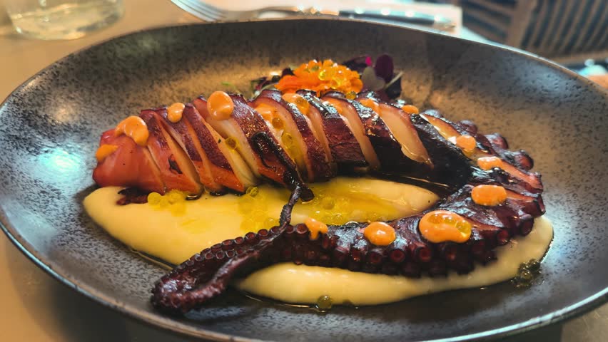 Pulpo a la brasa, grilled octopus served on a bed of mashed potatoes with red caviar and greens, a traditional Spanish dish. High quality 4k footage