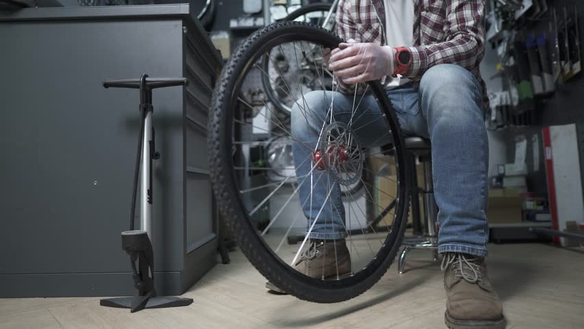 Mechanic repairing a bicycle wheel and tire in a dark workshop or bike store. Concept for maintenance, technical service, hobby, sport preparation, and small business work
