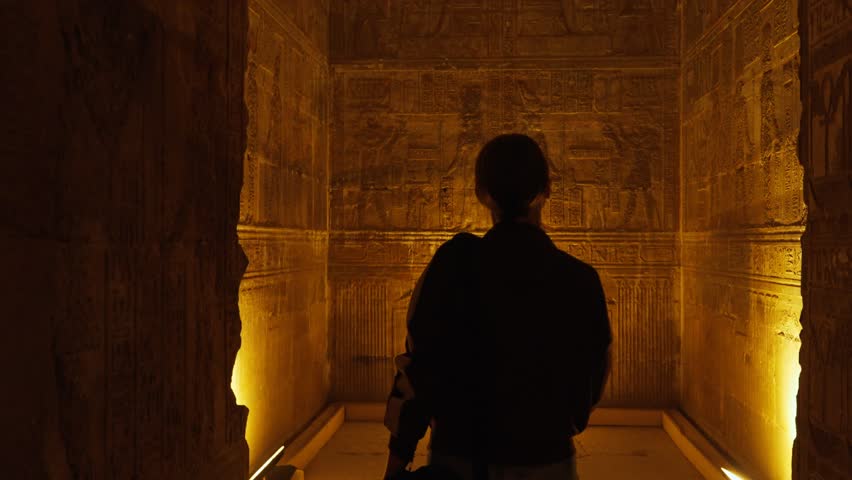 A female tourist admires the interior of the temple in Dendera or the temple of Hathor in Egypt. Ancient hieroglyphic carvings on the temple walls. The history of Egypt.