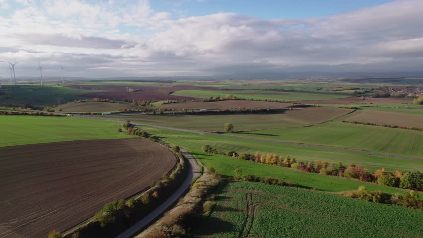 Aerial Farmland Landscape Under Cloudy Sky Showcasing Patchwork Fields, Winding Lane, Hedgerow And Autumnal Trees Drone Survey Captures Moody Light, Textured Soil, Deep Shadows