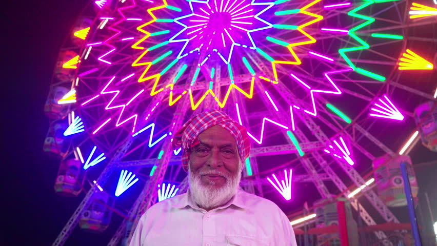Elderly Indian man wearing a traditional headscarf against the Ferris Wheel