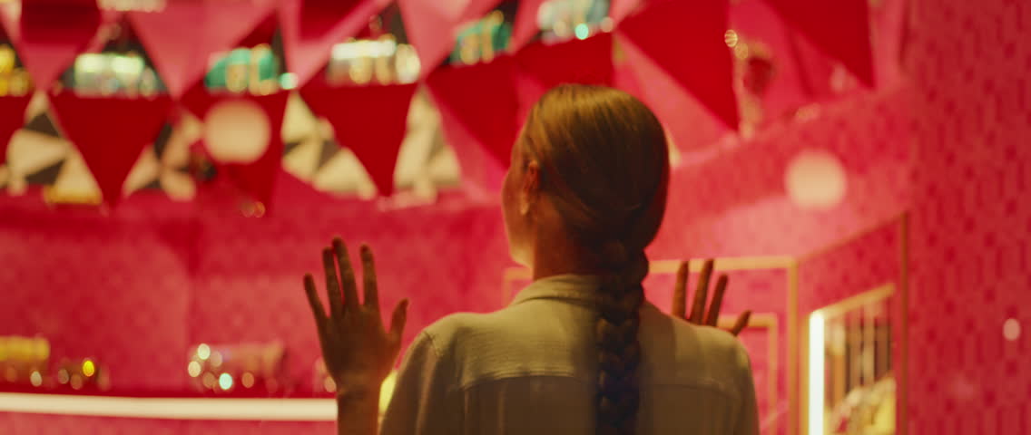 Woman standing before a shop window, hands raised in awe, mesmerized by the luxury items inside