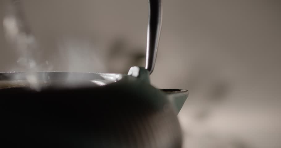 Hot cast iron teapot closeup over blurred background. Steam rising from the teapot during a traditional tea ceremony. Asian relaxation concept atmosphere.