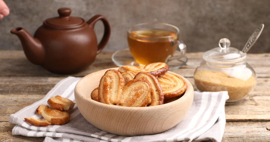 Woman taking palmier cookie at wooden table, closeup