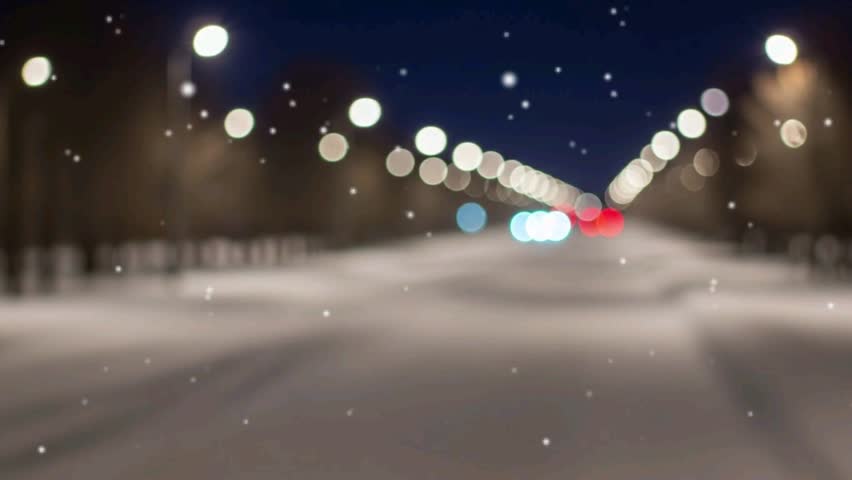 A blurry view of a snow-covered road at night, with falling snow and bokeh lights from streetlamps and vehicles, creating a dreamy atmosphere.