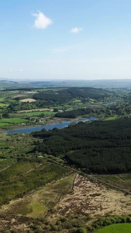 Scenic landscape of Ireland featuring green fields, forests, lakes, and distant windmills on a bright day.