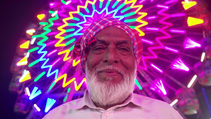Elderly Indian man wearing a traditional headscarf against the Ferris Wheel